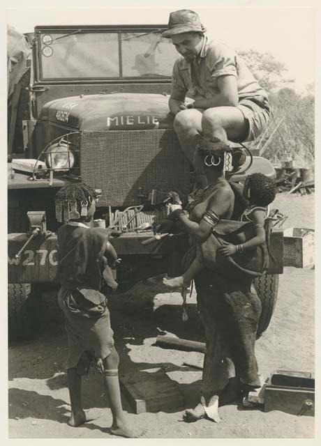 Casper Kruger sitting on headlight of the GMC; N!ai and a woman carrying a baby on her back below
























