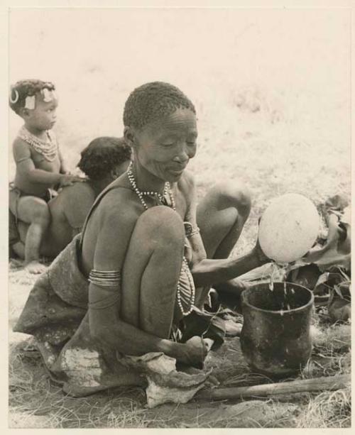 /Naoka, first wife of "Gao Medicine," emptying contents from an ostrich eggshell into a pot, with a child sitting on somebody's back behind her
























