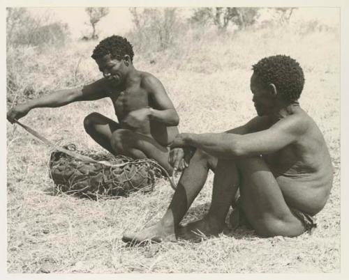 Man watching ≠Toma lining a carrying net with a small kaross to pack it with rattles, ostrich eggshells, etc.

























