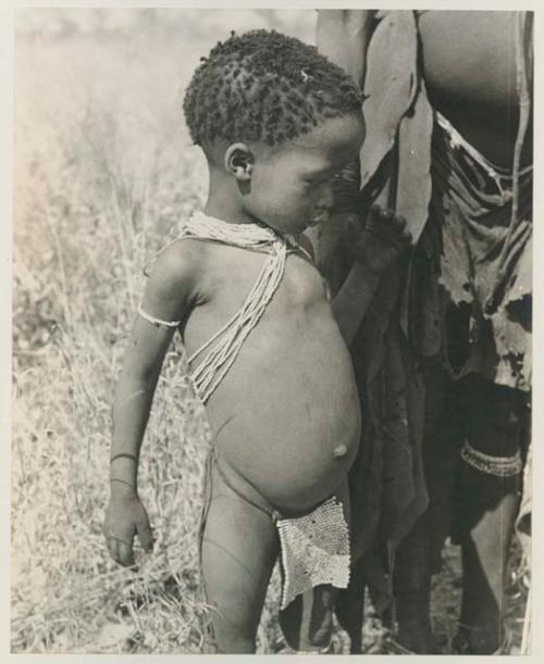 Norna standing beside a woman, showing her beaded modesty apron and strings of beads
























