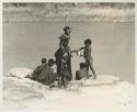 Boy handing a can to a woman at the water, with other people around








