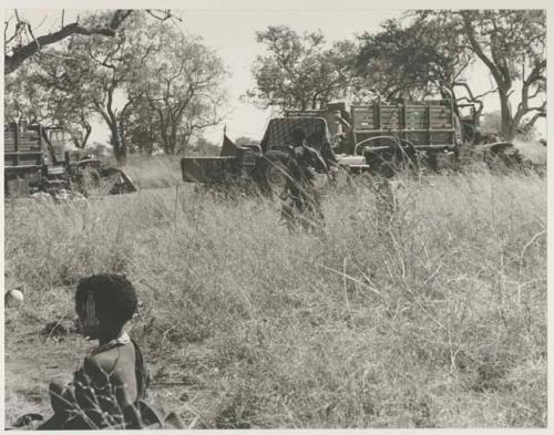 Ju/'hoansi walking with trucks in the background
