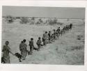 "Band moving": Band of people walking in a line, with the men in the front and the women in the back