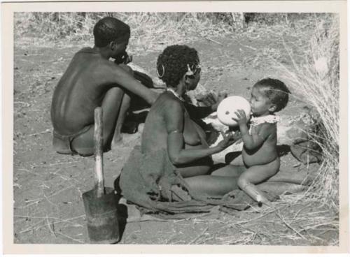 "Waterhole / Gwia": !Ungka (≠Toma's sister) with her daughter, Sa≠gai, sitting on her knees drinking from an ostrich eggshell; Tsamgao (Bau's husband) sitting beside her (print is a cropped image)