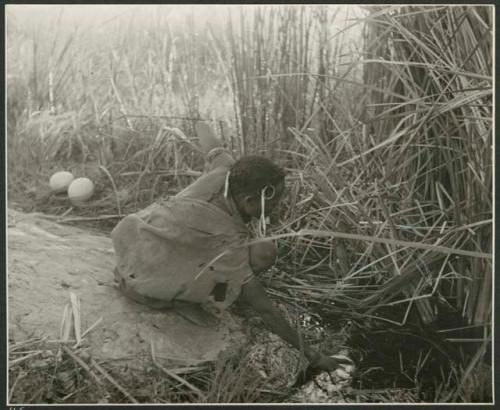 "Waterhole / Gwia": Woman filling an ostrich eggshell with water at a waterhole (print is a cropped image)