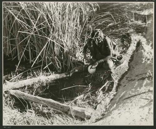 "Waterhole / Gwia": Woman filling an ostrich eggshell with water at a waterhole (print is a cropped image)