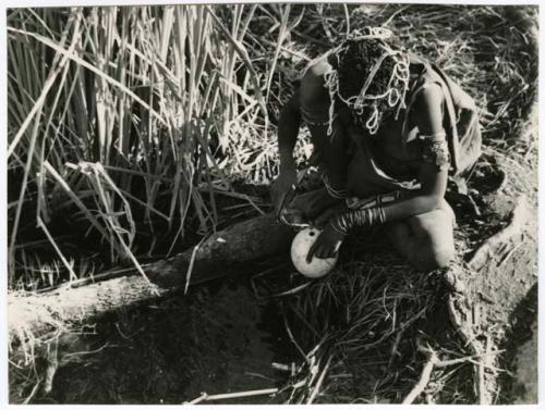 "Waterhole / Gwia": Woman filling an ostrich eggshell with water at a waterhole (print is a cropped image)