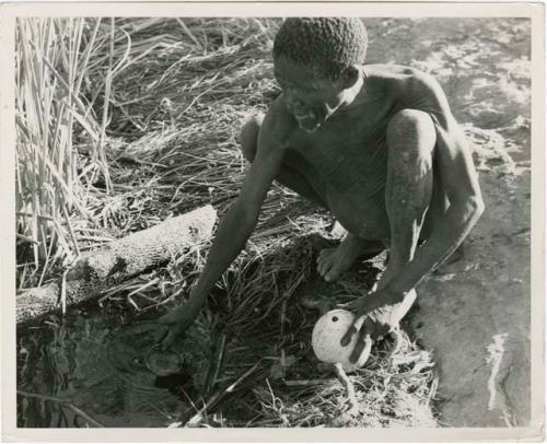 "Waterhole / Gwia": "Old /Gaishay" of Band 4 filling his //’ai [ostrich eggshell water container], (print is a cropped image)