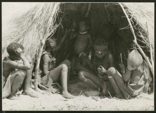 [No folder title]: Group of people sitting inside a skerm, shows skerm entrance and water-bag made from an animal stomach (print is a cropped image)