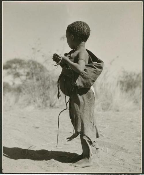 [No folder title]: Be, daughter of Bo, standing, with a piece of veldkos she gathered tied in her kaross (print is a cropped image)