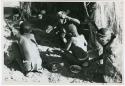 [No folder title]: Four people sitting around a fire, seen from behind (print is a cropped image)