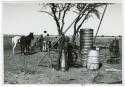 [No folder title]: Expedition members standing by a water trough; man with two horses (print is a cropped image)