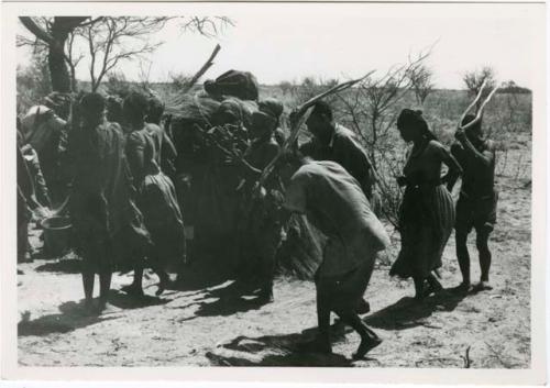 [No folder title]: Group of people performing the Eland Dance; group of women clapping; men holding wooden horns to their heads (print is a cropped image)