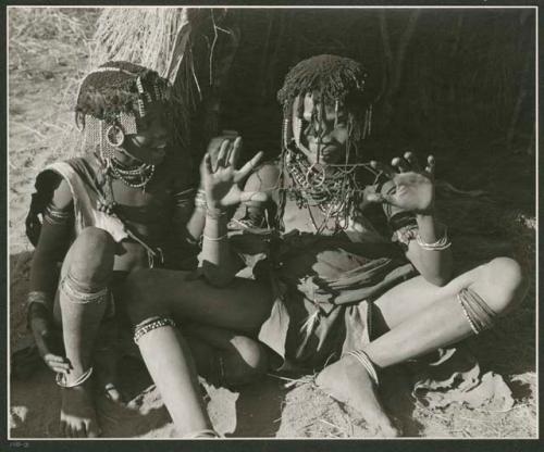 "Cats cradle": Two girls sitting in front of a skerm, one is making a "cat's cradle" (print is a cropped image)