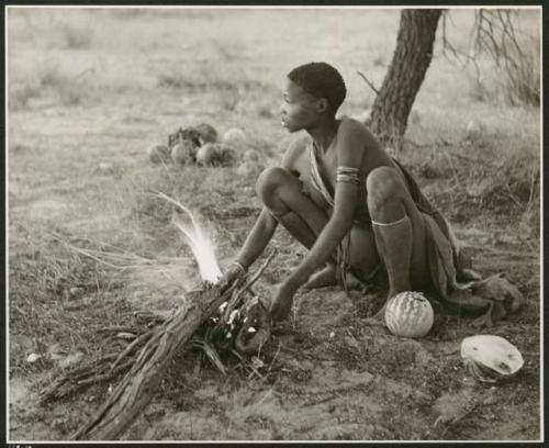 "'E', Chapter 9, 51": Woman squatting by fire, a melon beside her, settled for the night (print is a cropped image)