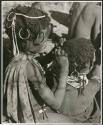 "Grooming & haircuts": Girl looking for lice in the hair of a smaller child (print is a cropped image)