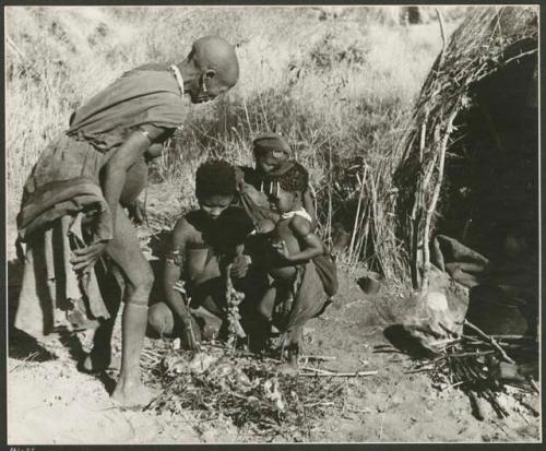 "Meat sharing": "Old /Gasa" and her daughter /Naoka (wife of "/Qui Hunter") looking at a pile of entrails lying on leaves and twigs in front of a skerm (print is a cropped image)