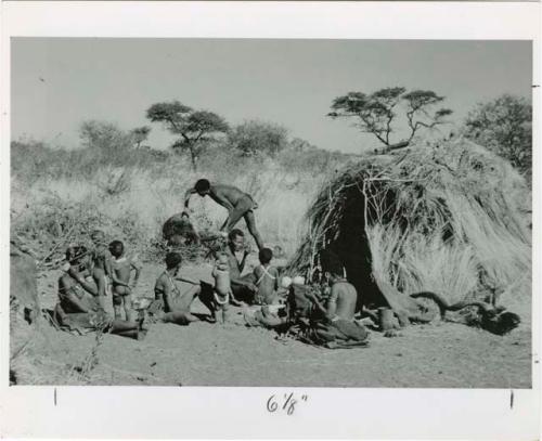 "Meat sharing": "Gao Medicine" bringing a quarter of meat in meat distribution to a group of people sitting in front of a skerm, including "Old ≠Toma" sitting in the middle of the group (print is a cropped image)