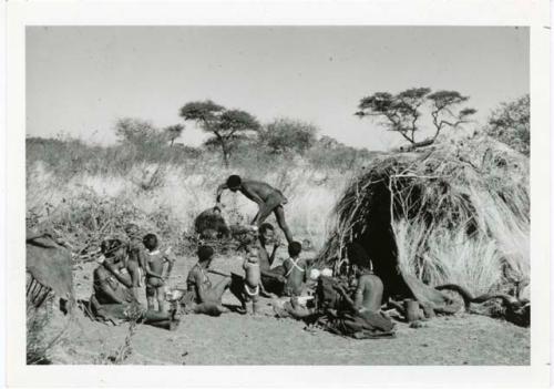 "Meat sharing": "Gao Medicine" bringing a quarter of meat in meat distribution to a group of people sitting in front of a skerm, including "Old ≠Toma" sitting in the middle of the group (print is a cropped image)