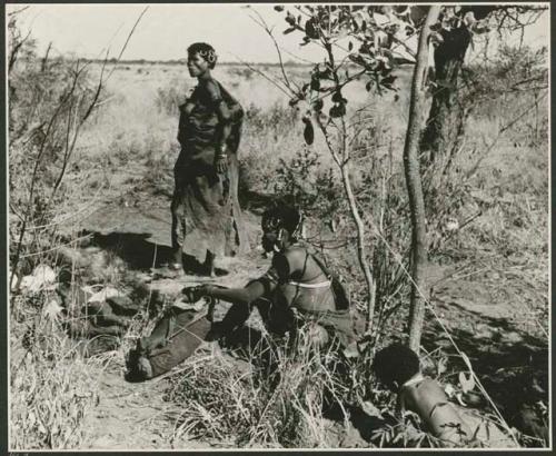 "Move": //Kushay standing in her living place, with another woman squatting nearby holding a large animal skin bag full of nuts