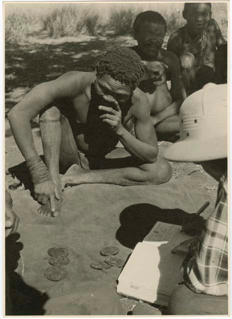 "Oracle disk": Men practicing oracle disc divination, with Lorna Marshall taking notes (print is a cropped image)