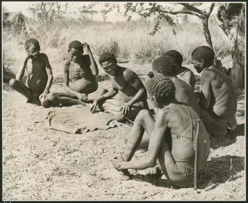 "Oracle disk": Man reading oracle disks, and a group of men sitting and watching him (print is a cropped image)