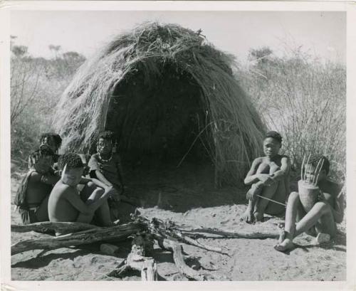 "N!ai and /Gunda": Little N!ai" and /Gunda (son of Khuan//a and her former husband) sitting by their skerm with their wedding party, including Tsamgao (son of ≠Toma and !U), ≠Gisa (daughter of ≠Gao and Khwo//o-/Gasa), Xama (daughter of "Gao Helmet" and //Kushay), ≠Gao (son of Gau and Be), and a boy playing the //guashi (print is a cropped image)