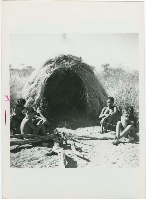 "N!ai and /Gunda": Little N!ai" and /Gunda (son of Khuan//a and her former husband) sitting by their skerm with their wedding party, including Tsamgao (son of ≠Toma and !U), ≠Gisa (daughter of ≠Gao and Khwo//o-/Gasa), Xama (daughter of "Gao Helmet" and //Kushay), ≠Gao (son of Gau and Be), and a boy playing the //guashi