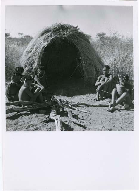 "N!ai and /Gunda": Little N!ai" and /Gunda (son of Khuan//a and her former husband) sitting by their skerm with their wedding party, including Tsamgao (son of ≠Toma and !U), ≠Gisa (daughter of ≠Gao and Khwo//o-/Gasa), Xama (daughter of "Gao Helmet" and //Kushay), ≠Gao (son of Gau and Be), and a boy playing the //guashi