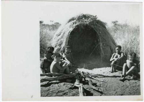 "N!ai and /Gunda": Little N!ai" and /Gunda (son of Khuan//a and her former husband) sitting by their skerm with their wedding party, including Tsamgao (son of ≠Toma and !U), ≠Gisa (daughter of ≠Gao and Khwo//o-/Gasa), Xama (daughter of "Gao Helmet" and //Kushay), ≠Gao (son of Gau and Be), and a boy playing the //guashi (print is a cropped image)