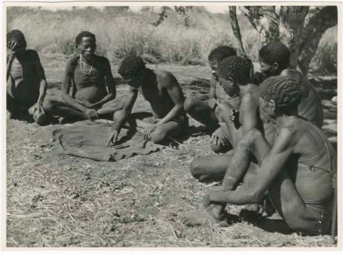 "Oracle disk": Man reading an oracle disk, and a group of men sitting and watching him (print is a cropped image)