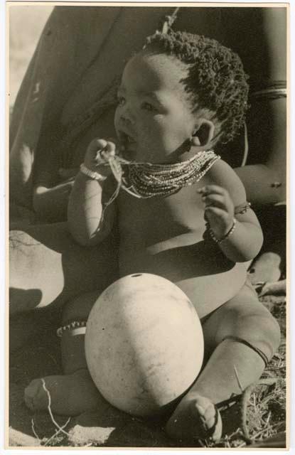 "Ostrich egg shell": Baby (child of ≠Gao, leader of Band 10, and Bau, his first wife) sitting next to an ostrich eggshell (print is a cropped image)