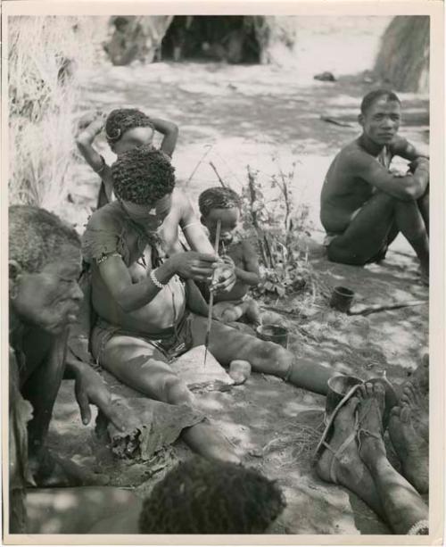 "Ostrich egg shell bead making": !U sitting with a group of people, drilling holes in ostrich eggshell beads (print is a cropped image)