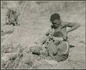 "Ornaments & beads": Woman of Band 11 putting an ostrich eggshell headband on her child (print is a cropped image)