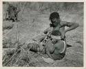 "Ornaments & beads": Woman of Band 11 putting an ostrich eggshell headband on her child (print is a cropped image)