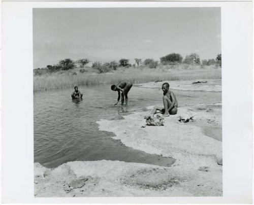 "Pan": Three men by the water, one sitting on the sand, one leaning over with his hand in the water and one bathing (print is a cropped image)