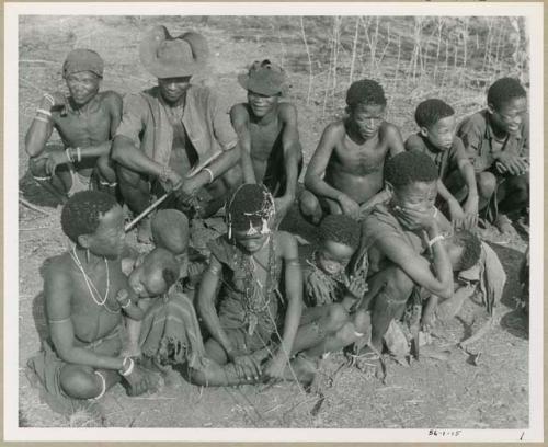 [No folder title]: Unidentified Ju/'hoan man, Herero man wearing a hat, unidentified Ju/'hoan man (all three visiting from Kai Kai), ≠Toma, Tsamgao (his son), and /Gunda (husband of !Nai) sitting in the back row; and !Ungka (≠Toma's sister from Kai Kai) with Sa≠gai and ≠Kham (her two children), an unidentified girl, !Ungka (Norna) (daughter of ≠Toma and !U), and !U with Di//kaho (her baby) sitting in the front row (print is a cropped image)