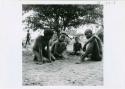 [No folder title]: Four boys sitting, playing /Ui (the counting game), with the boy on the right holding a slender white stick (print is a cropped image)