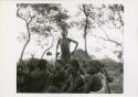 [No folder title]: Dancer stands behind a group of women sitting (print is a cropped image)