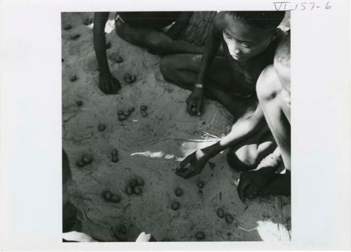 [No folder title]: Group of boys playing /Ui (the counting game), with nuts in the holes in the sand, view from above (print is a cropped image)