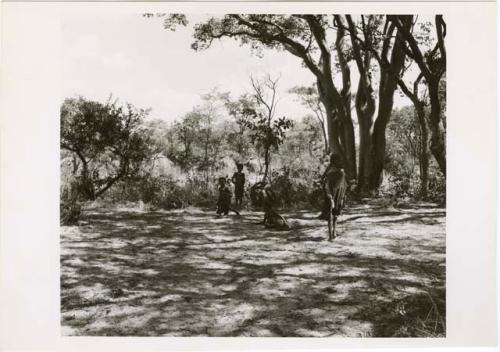 [No folder title]: Woman carrying a child in a sling on her back walking toward a group of women and children, with her back to the camera (print is a cropped image)