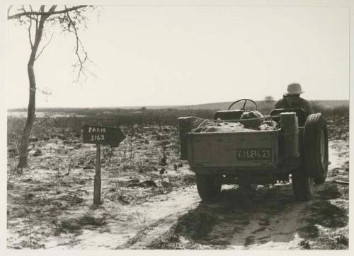 Expedition Jeep driving past sign showing 5162 miles to Paris