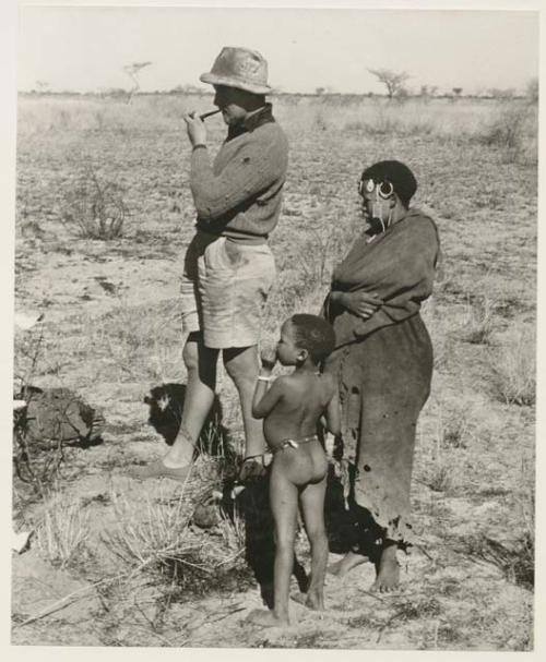 Group of people standing around the Jeep, including !Ungka wearing a dress, "Old Gau" wearing a shirt, and expedition members