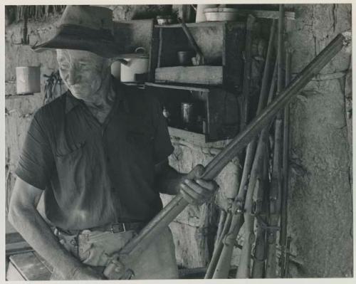 Thomas Hardbattle standing in his store-room and holding a gun