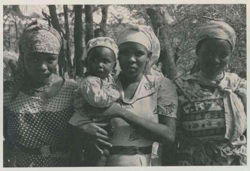 Three women standing, one holding a baby