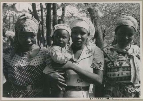 Three women standing, one holding a baby