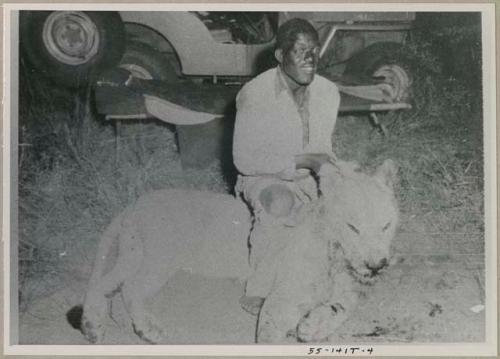 Simon Molamo sitting over a dead lion, holding the lion's head