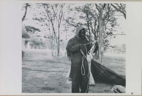 Kernel Ledimo wearing clothing and head covering to protect against tsetse flies, and untangling tent ropes


