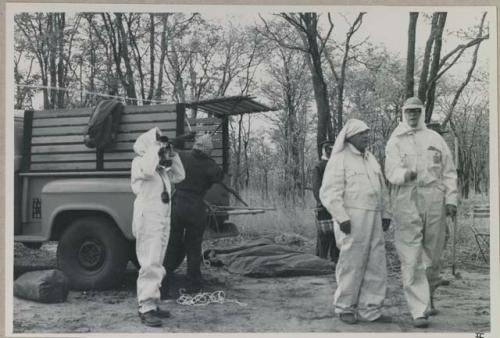 Lorna Marshall taking a photograph of Nicholas England and Laurence Marshall walking, and all are wearing clothing and head coverings to protect against tsetse flies


