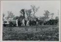 Expedition members standing near line of trucks and wearing clothing and head coverings to protect against tsetse flies
